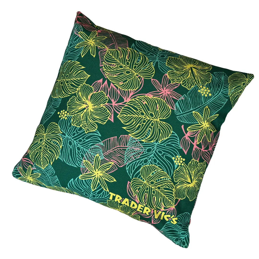 A square decorative throw pillow featuring a tropical leaf and flower pattern in neon yellow, pink, and teal on a dark green background, with the text 'TRADER VICS' printed near the bottom.