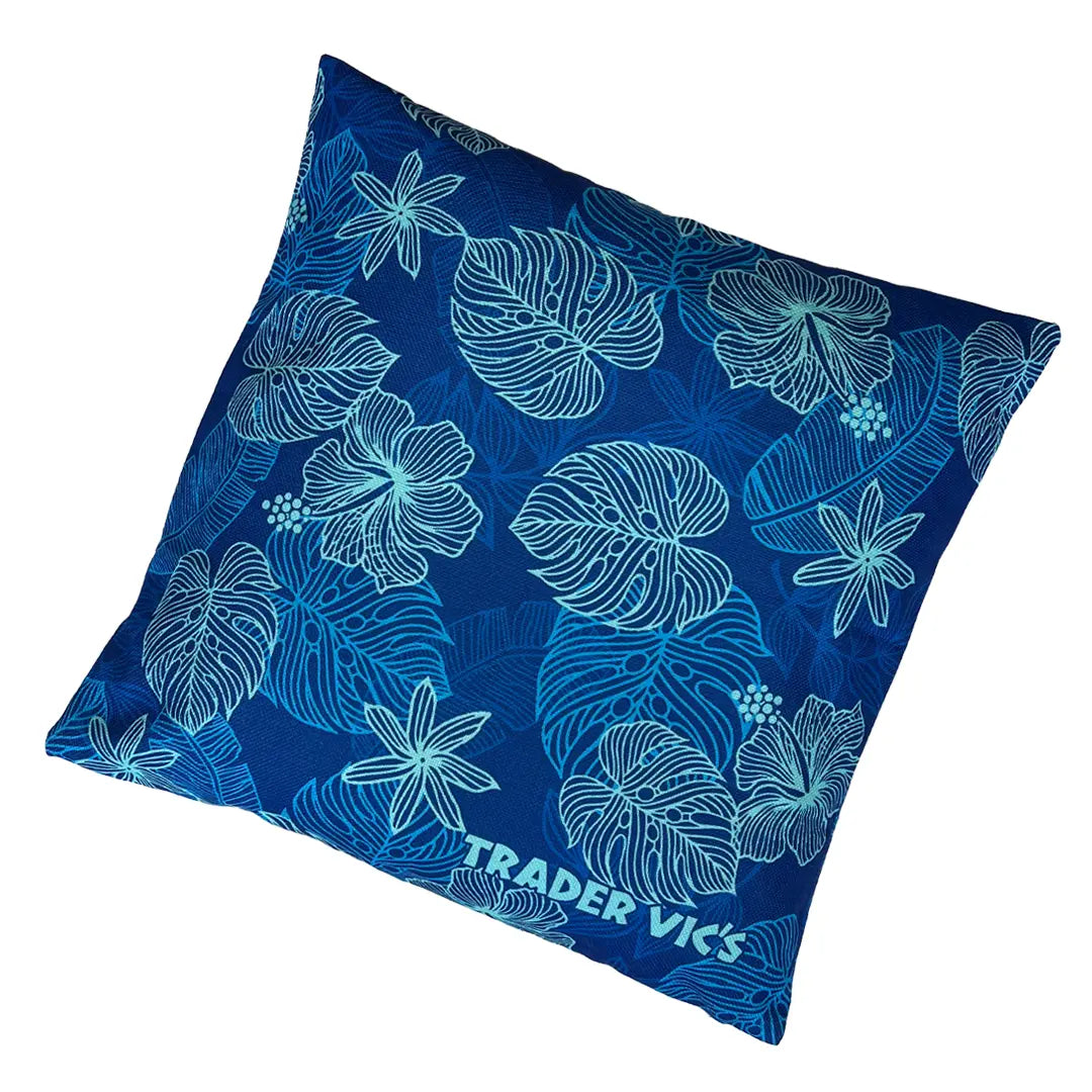 A square blue throw pillow featuring a white tropical floral and leaf pattern, with the brand name 'TRADER VICKS' printed in white near the bottom corner, set against a plain white background.