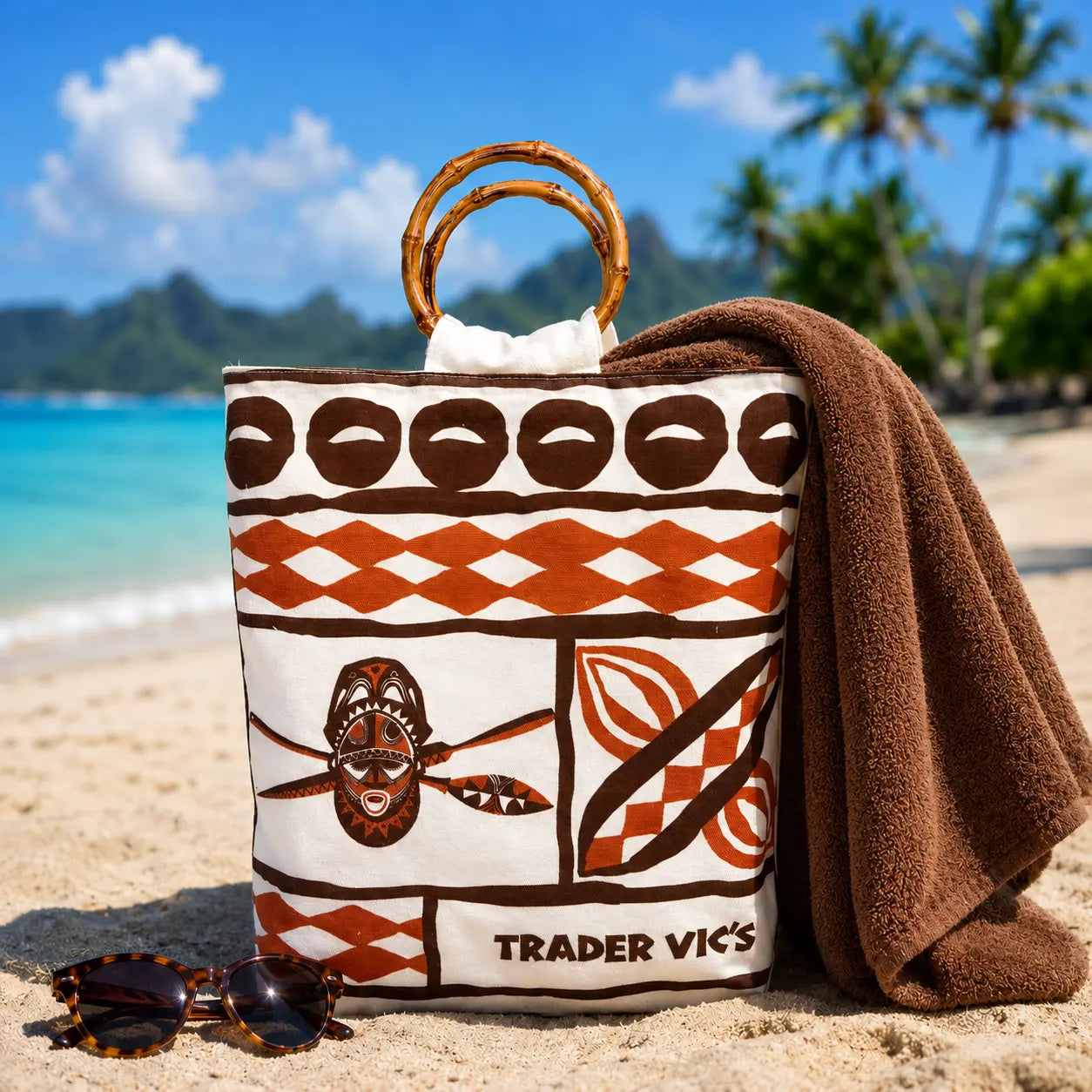 A white canvas tote bag with a brown and orange tapa pattern, featuring bamboo handle and the 'TRADER VIC'S' logo printed at the bottom.