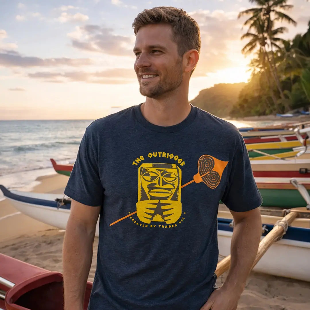 Man wearing a navy blue t-shirt with a yellow graphic design on a beach with boats and sunset in the background