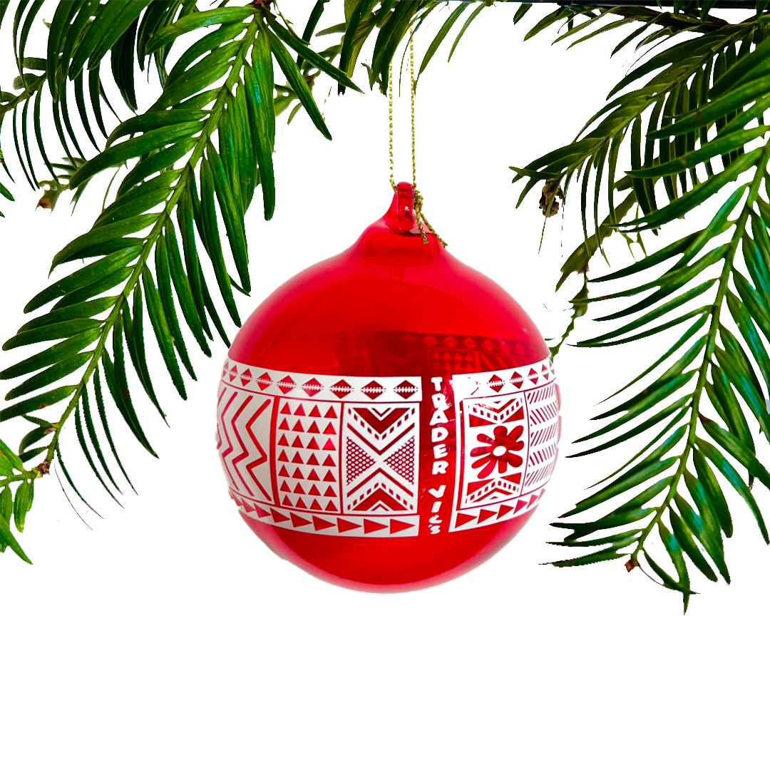 Red Christmas ornament with white patterns hanging on a green branch