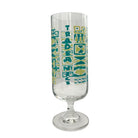 A clear glass goblet with a stylized teal and yellow-green geometric graphic pattern featuring the word 'TRADE' vertically, set against a plain white background.
