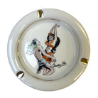 A round ceramic ashtray with a glossy cream-white glaze, featuring a hand-painted illustration of Trader Vic's vintage cocktail menu scene.