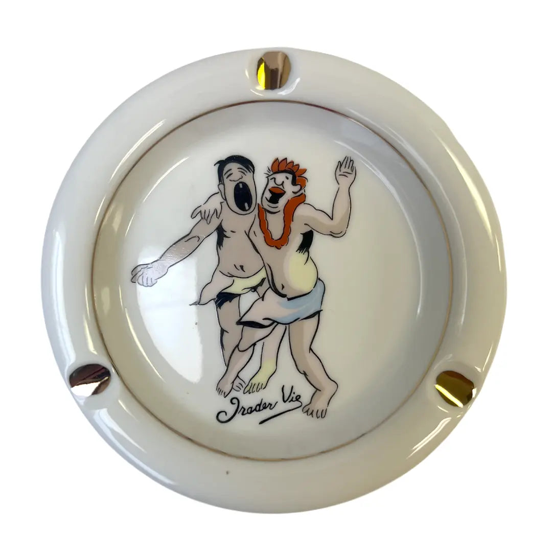A round ceramic ashtray with a glossy cream-white glaze, featuring a hand-painted illustration of Trader Vic's vintage cocktail menu scene.