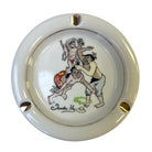 A round ceramic ashtray with a glossy cream-white glaze, featuring a hand-painted illustration of Trader Vic's vintage cocktail menu scene.
