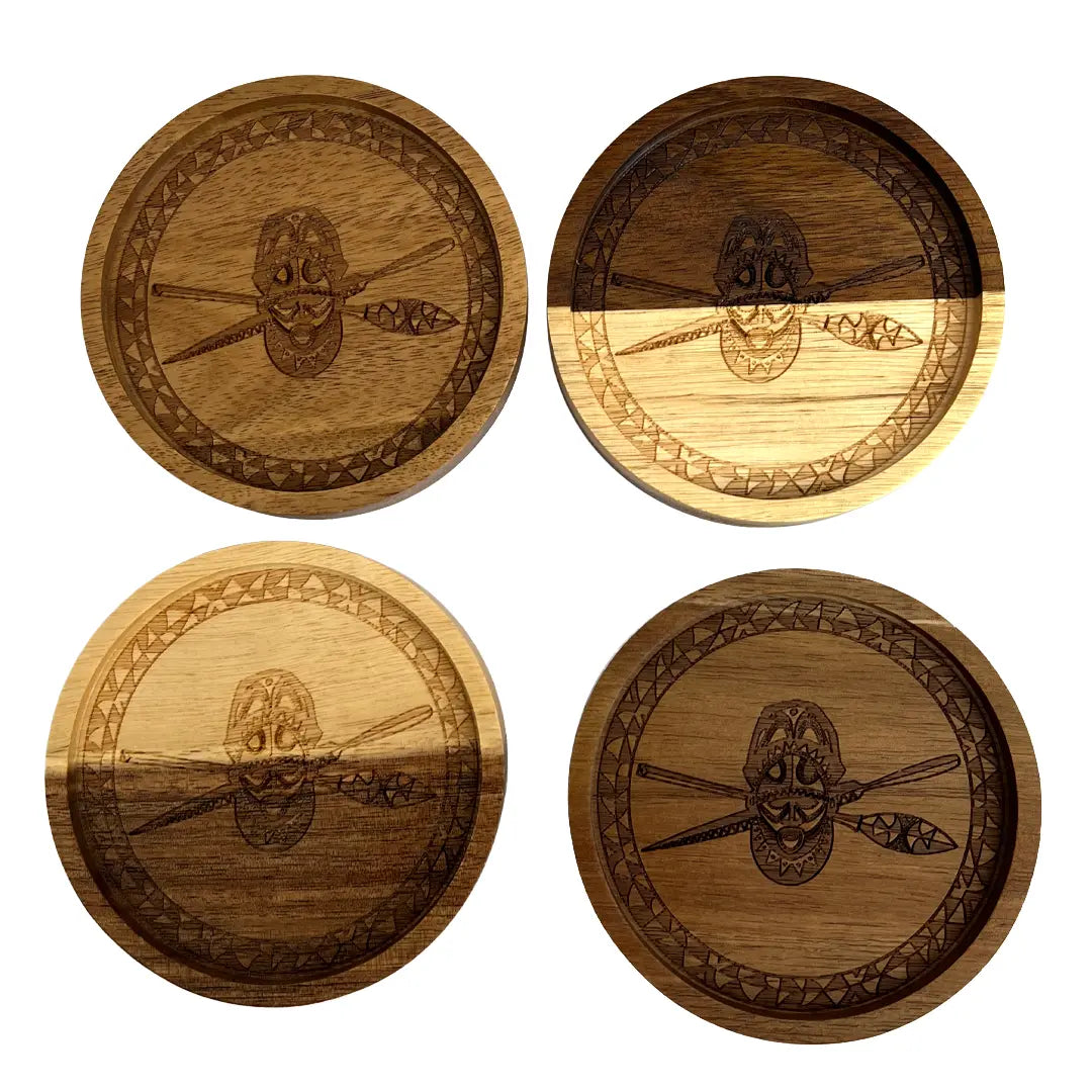 Four round wooden coasters arranged in a 2x2 grid on a white background. Each coaster features a dark engraved tribal-style face with crossed spears and a geometric border.