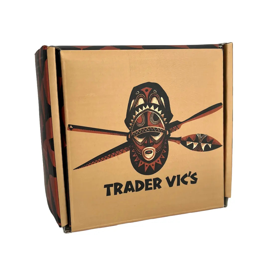 A square cardboard box with a brown kraft-paper front, featuring a stylized black and red tribal mask graphic and the text 'TRADER VIC'S' printed below. The sides of the box have a dark red and black patterned design, shown on a plain white background.