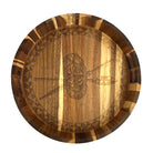 A round wooden serving tray with a hand-tooled shield and spear motif in the center, featuring a striped natural wood pattern around the rim, shown on a solid white background.
